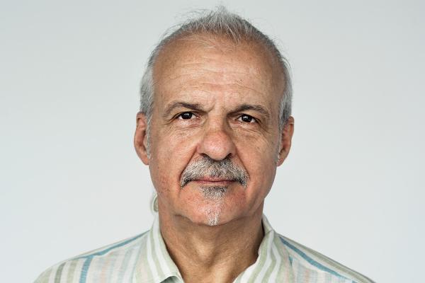 Oudere man met wit haar en witte snor kijkt met neutrale blik recht in de camera